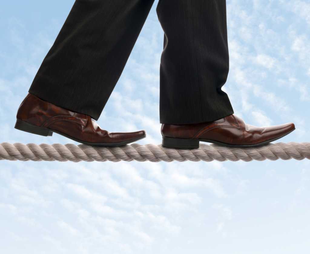 executive walking the tight rope with sky and clouds in background
