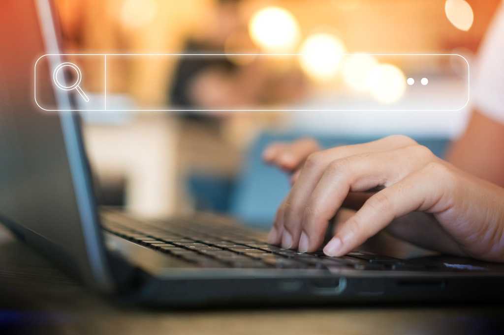 A conceptual browser search bar overlays a laptop with a user's hands on the keyboard.