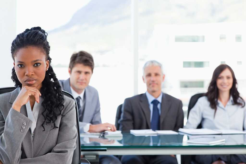 businesswoman sitting with her hand on her chin in front of her team in a meeting room151016166