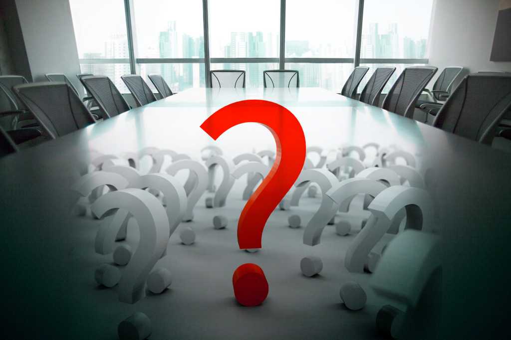 Empty seats in a board room with question marks.