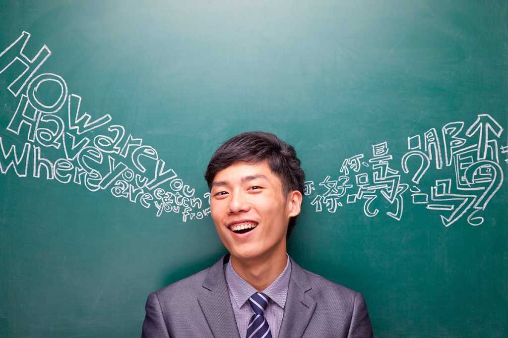 A man in front of a chalkboard, showing English language on the left and Chinese on the right.