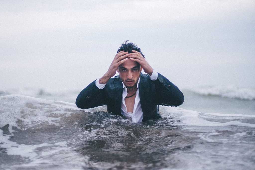 disheveled business man emerges from the ocean, holding his head