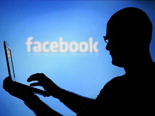 A man is silhouetted against a video screen with a Facebook logo