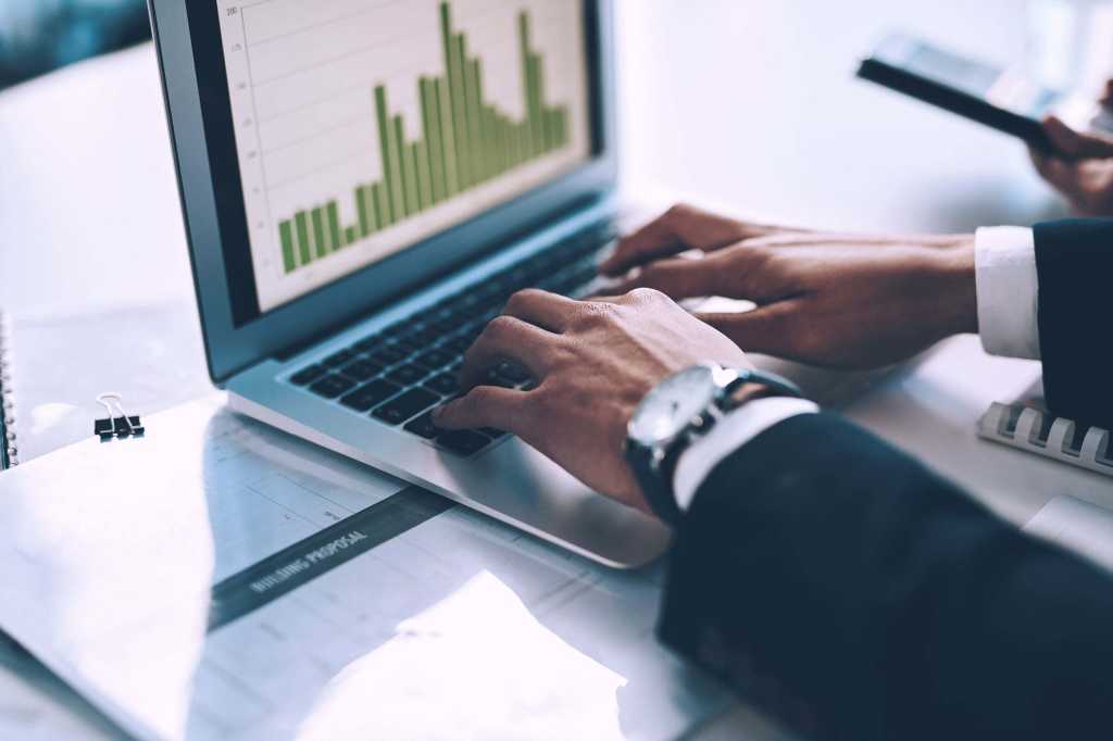 Hands type on the keyboard of a laptop displaying bar chart data / metrics / analytics.