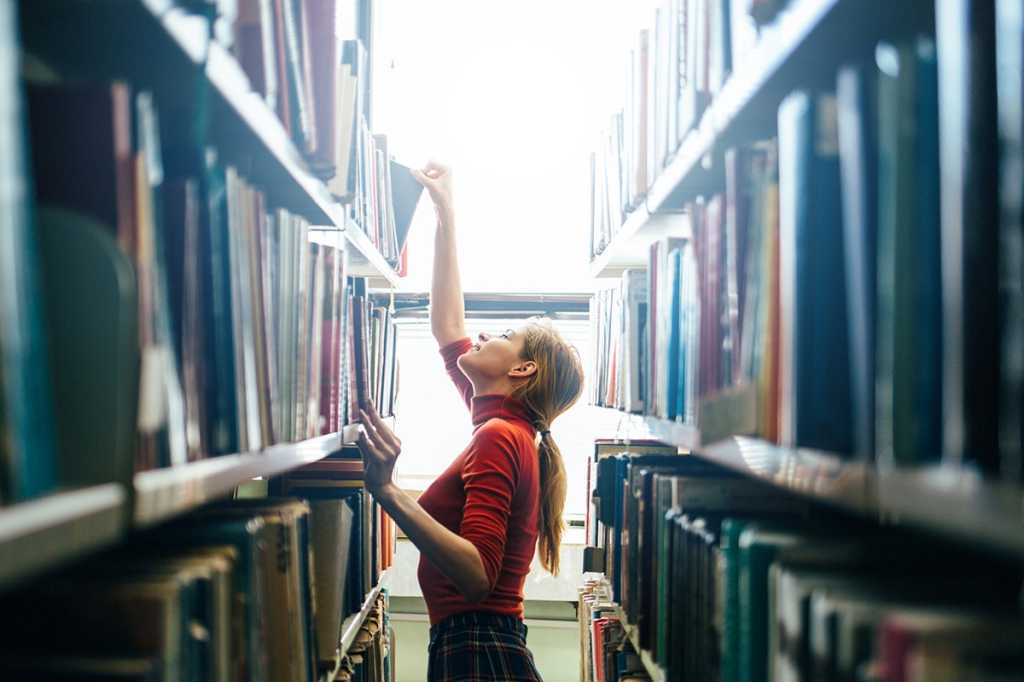 a woman takes a book from a shelf in a library or archive