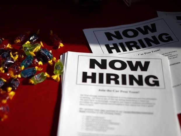 Leaflets that say Now Hiring lie on a table at a job fair