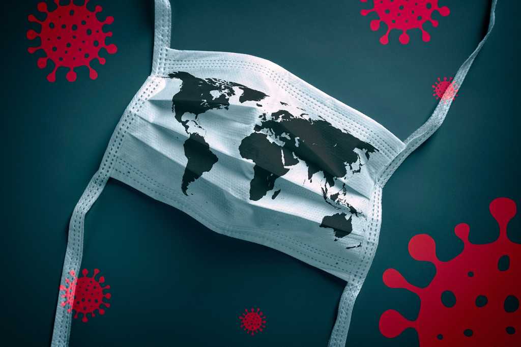 A protective face mask printed with a world map is surrounded by models of viral cells.