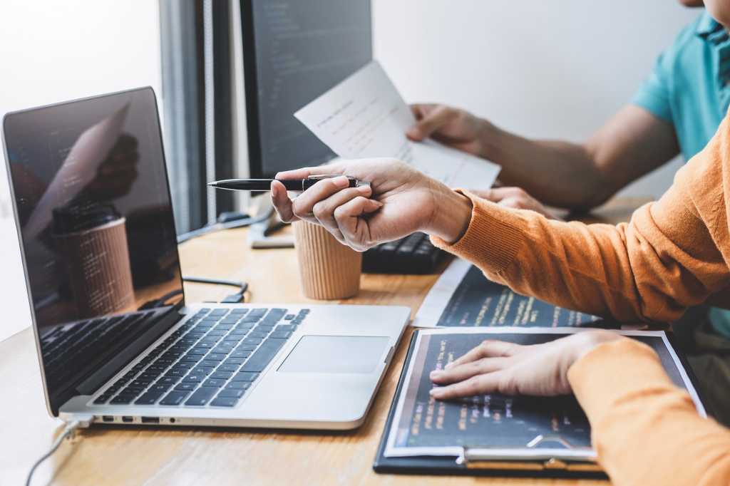 Two developers / programmers collaborate as they review code via laptop display.