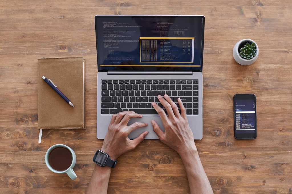 Hands type on a laptop keyboard with lines of code visible on the display.