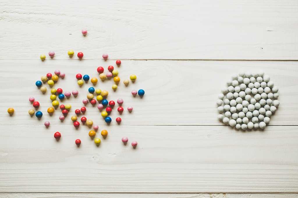 a scattered pile of multicolored pellets beside a unified grouping of all white pellets
