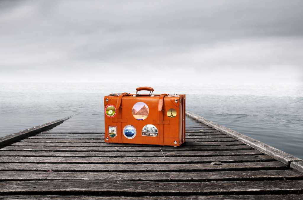 outsourcing suitcase with travel stickers at edge of dock