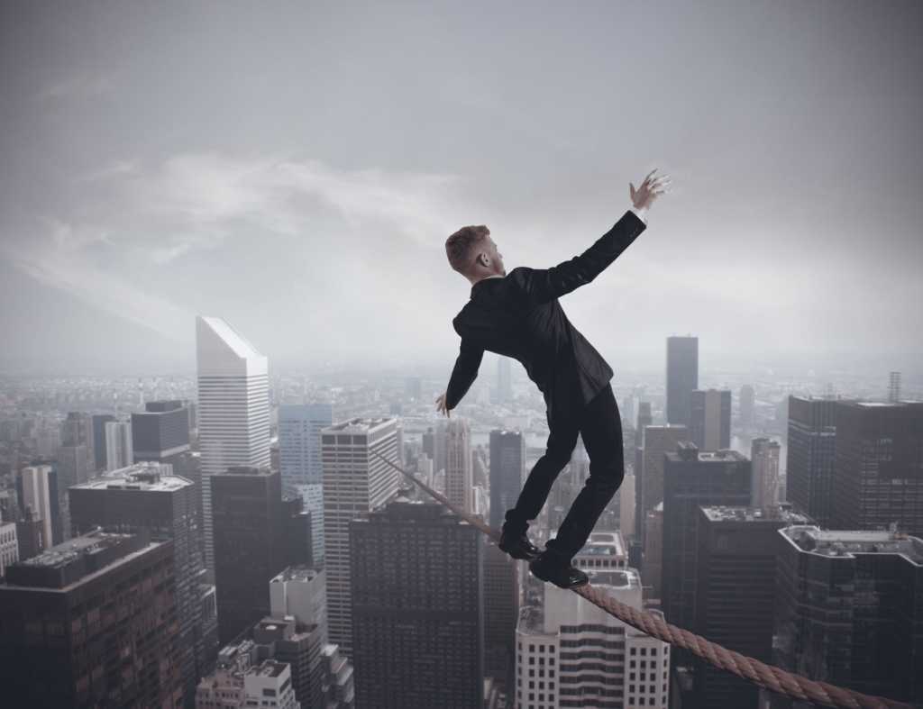 Young executive man balancing on tight rope over city buildings