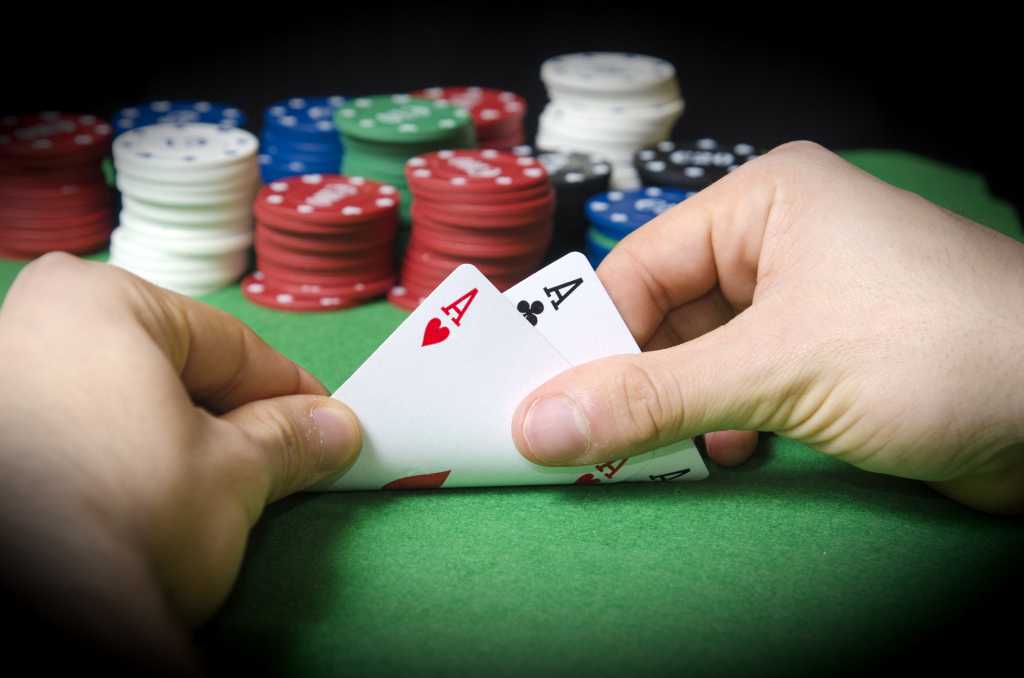 Hands holding a pair of aces at poker table
