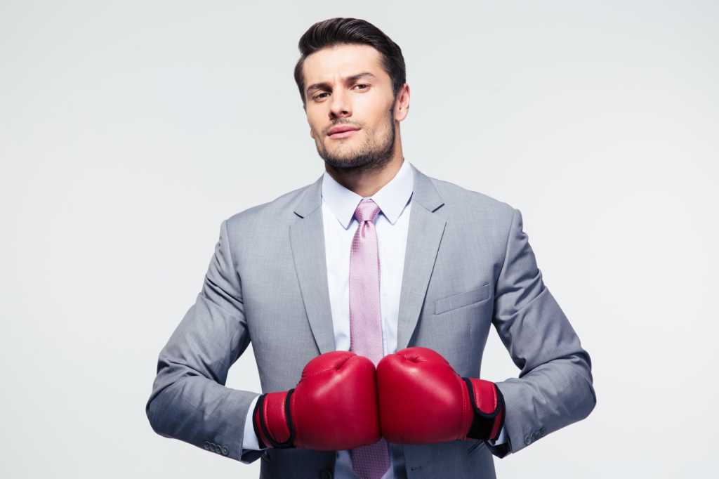 Man in gray suit wearing red boxing gloves looking for a fight