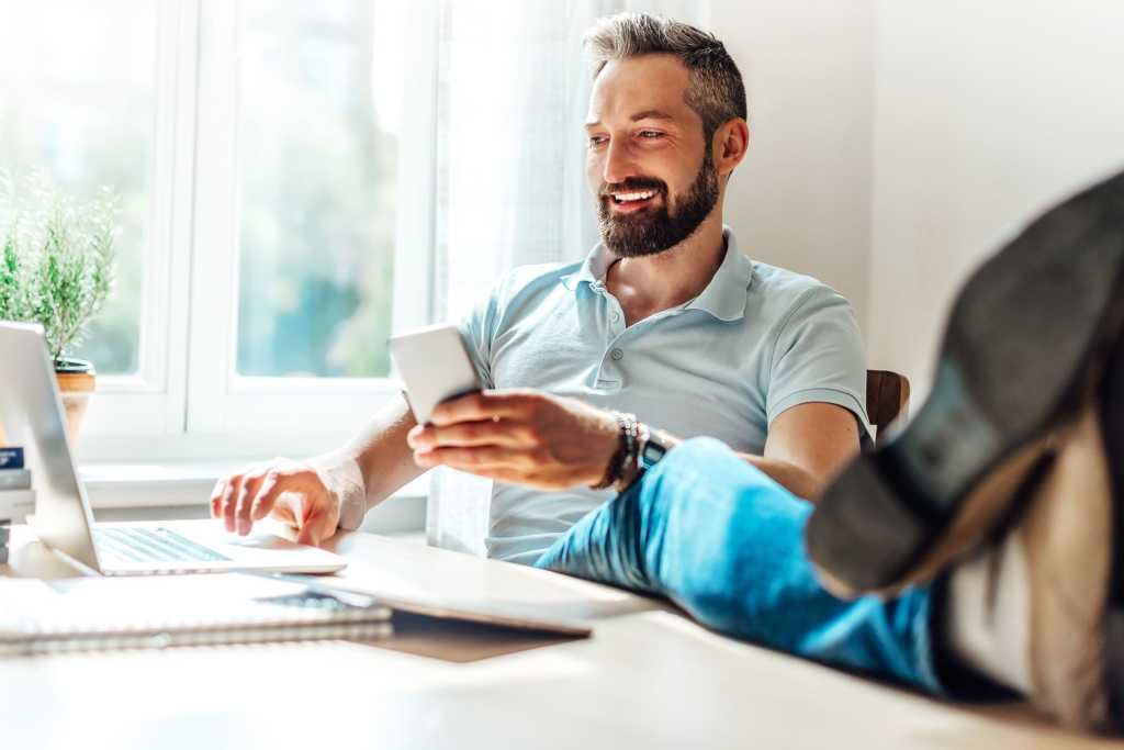 Casual man with beard seated at home office with smart phone