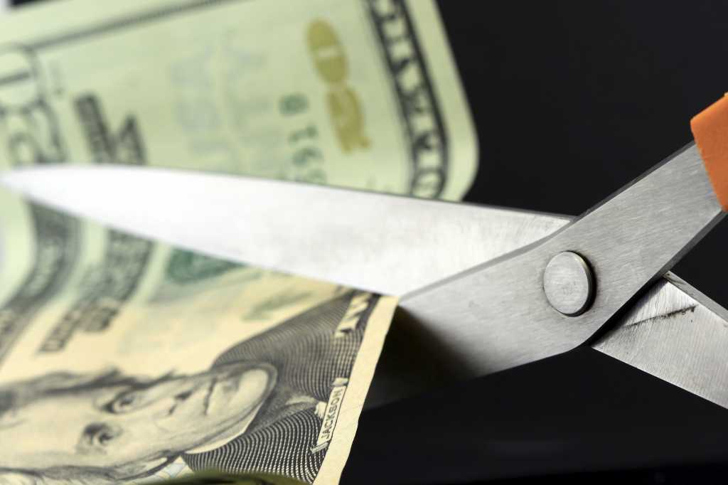 scissors cutting paper currency - reducing funds - cutting budget - decreasing finances
