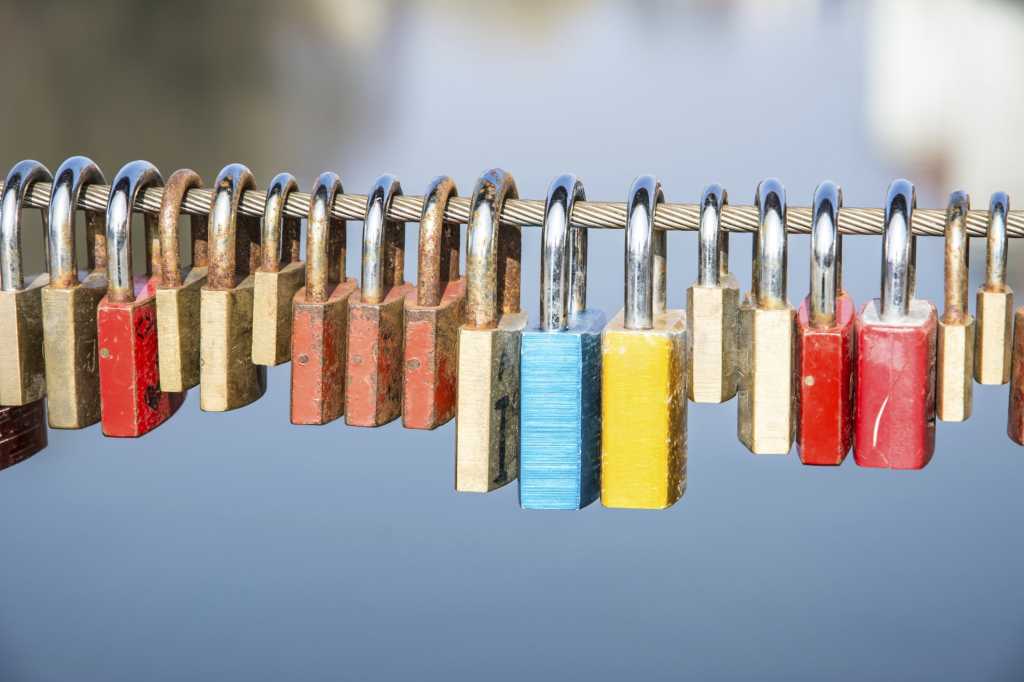 Row of colorful padlocks hanging on cable with water in background