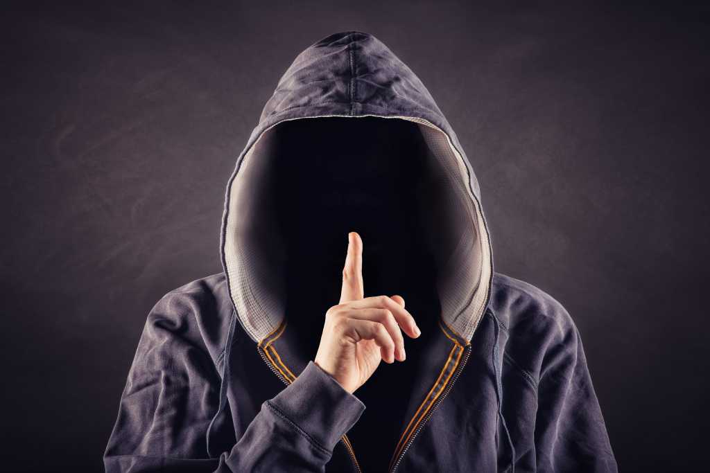 Hacker in hoodie holding up finger to be quiet secret