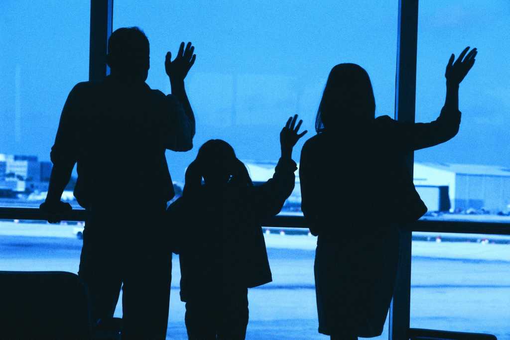 Family in silhouette waving goodbye at airport