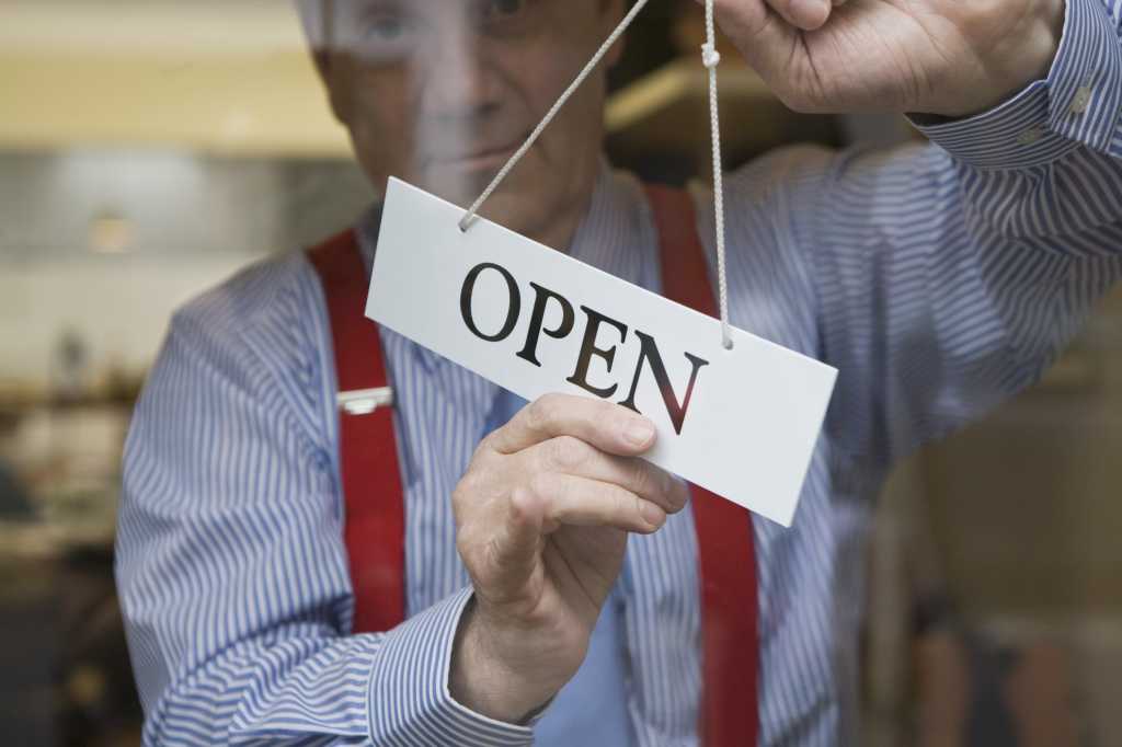 man in red suspenders standing at window with open sign