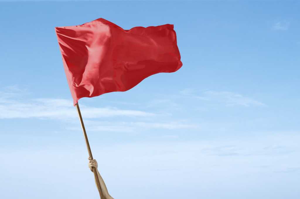 Arm waving red flag against blue sky