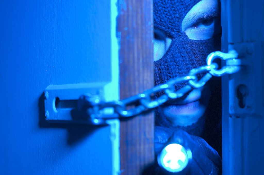 Closeup of burglar criminal trying to break in chain locked door