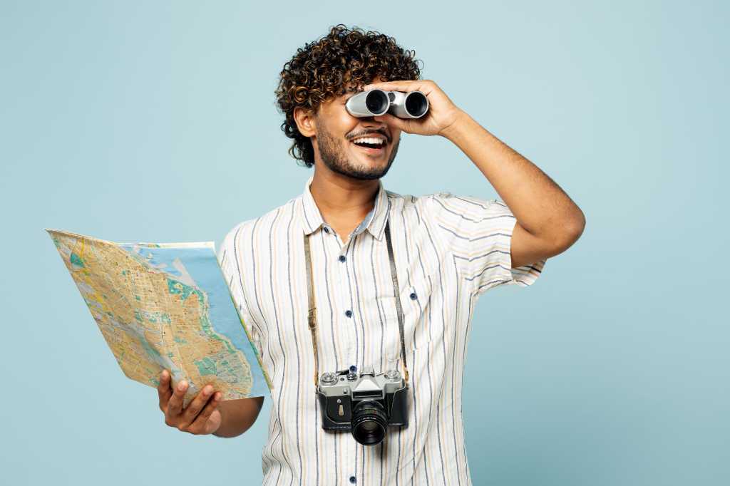 Viewing, surveying, looking ahead. Young man with binoculars and map in hand.