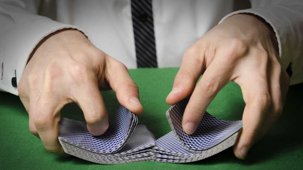 A close up photograph of a man's hands shuffling a deck of cards.