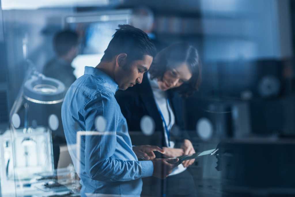 Two people review information on a tablet in an office workspace.