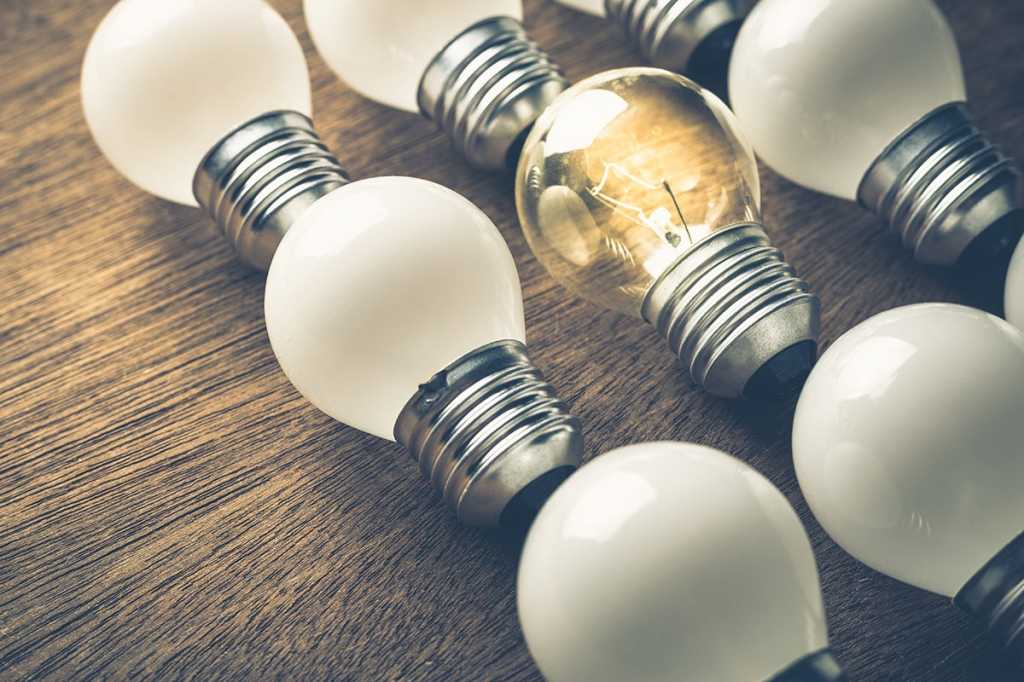 one lightbulb glowing among a pack of unlit bulbs