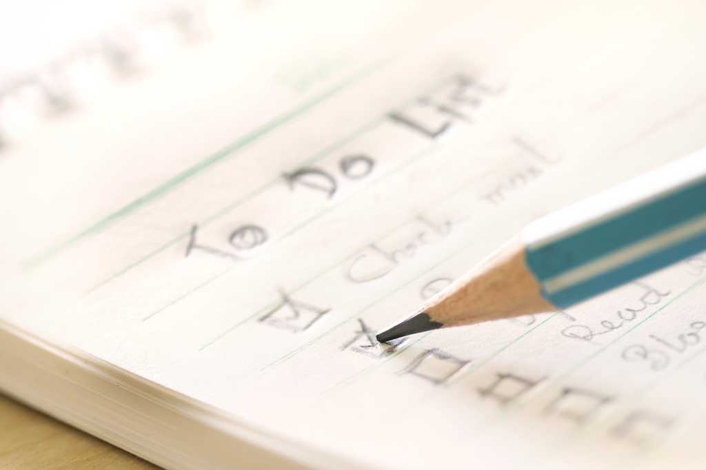 To-do list. A green pencil checking off items on a paper to-do list.