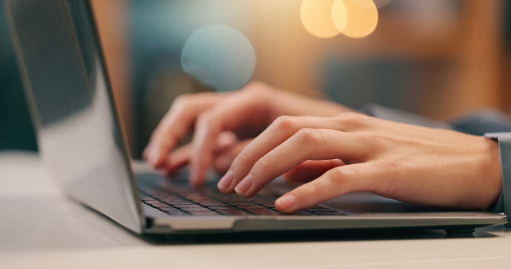 Hands typing at a laptop keyboard, soft focus background.