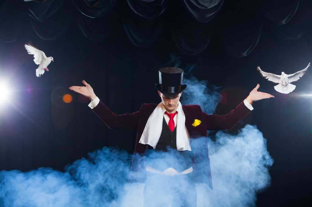 Magician with two flying white Doves on a black background shrouded in mysterious blue smoke