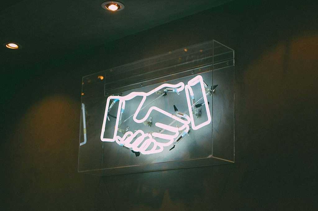 Neon sign > handshake / deal / agreement / partnership / team / merger