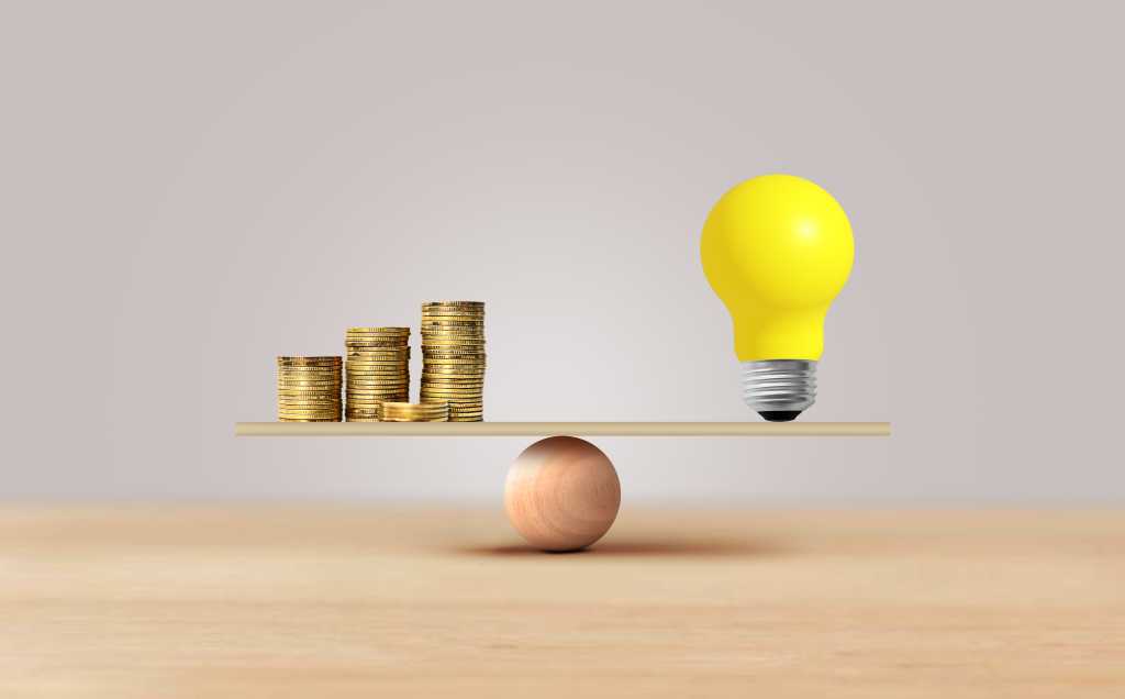 Light bulb anLight bulb and coins stacked balancing scale, investment in ideas.d coins stacked balancing scale, investment in ideas.