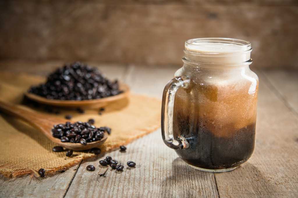 A mason jar of cold nitro coffee sits beside a pile of fresh espresso beans.