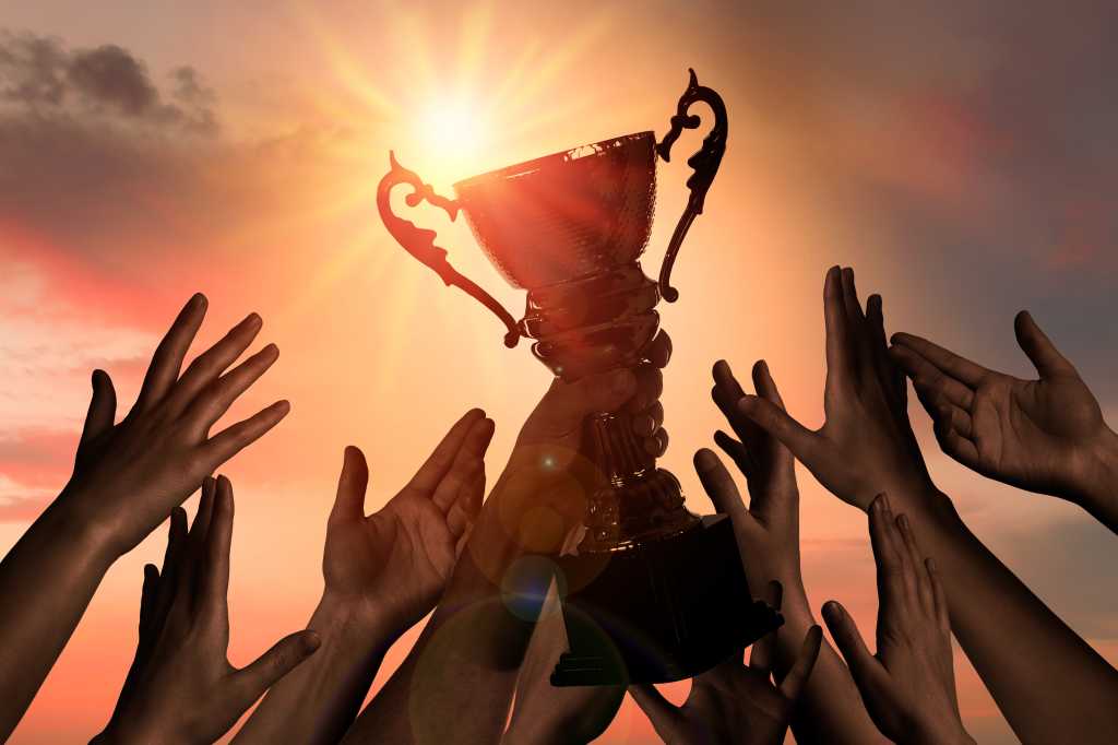 Gold trophy cup help up against shining sun as many hands reach for the prize.