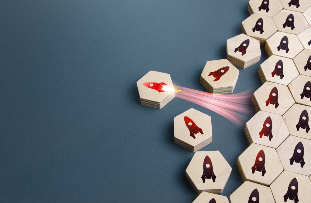 A wooden tile picturing a single red rocket breaks away from a line of others that are all the same. Blast off, breakthrough technology, choosing the best.