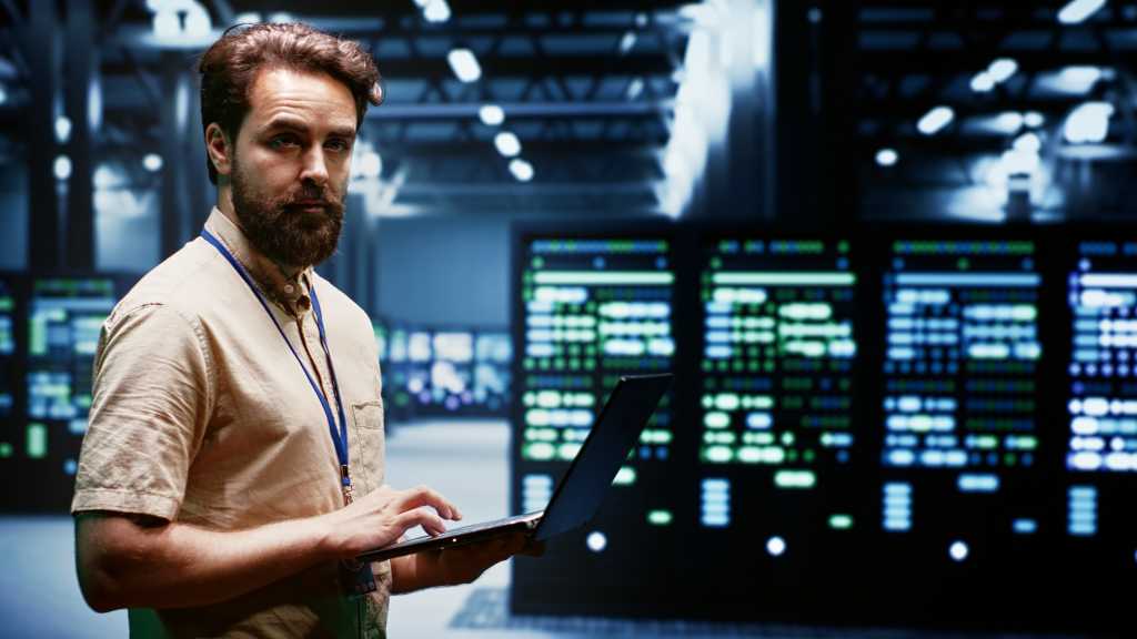 Experienced engineer writing data center disaster recovery plan on laptop to provide rapid restoration of service, limiting disruption and minimizing interruptions to normal operations