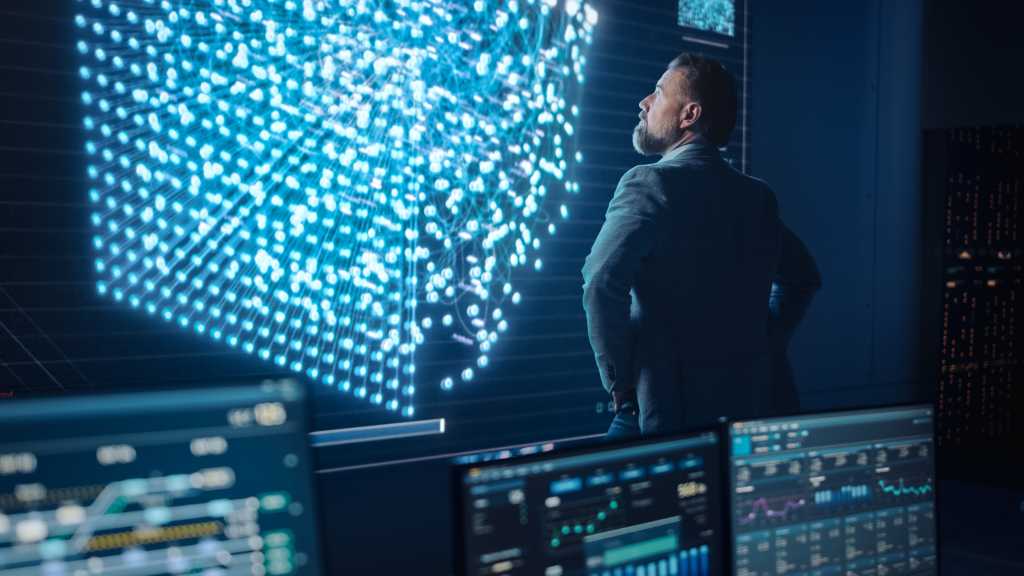 Middle Aged Bearded Senior Project Manager Stands Next to Big Screen with Neural Network. Professional Computer Data Science Engineer Work in a System Control and Monitoring Telecommunications Office