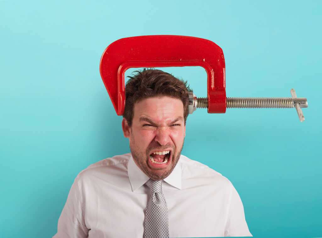 Groaning businessman with a giant red vise on his head. Headache concept. Painful squeeze.