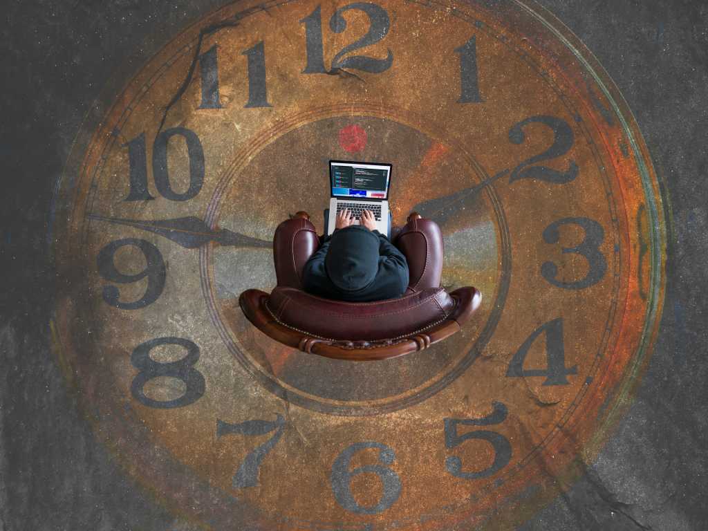 Man in easy chair on laptop with a brown analog clock image on the floor