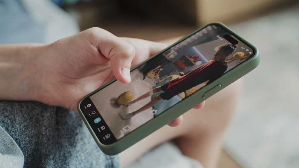 2503867677 Smartphone application with various video content displayed on phone screen. Close up of teenager scrolling and watching social media feed with short videos using mobile phone while sitting on sofa.