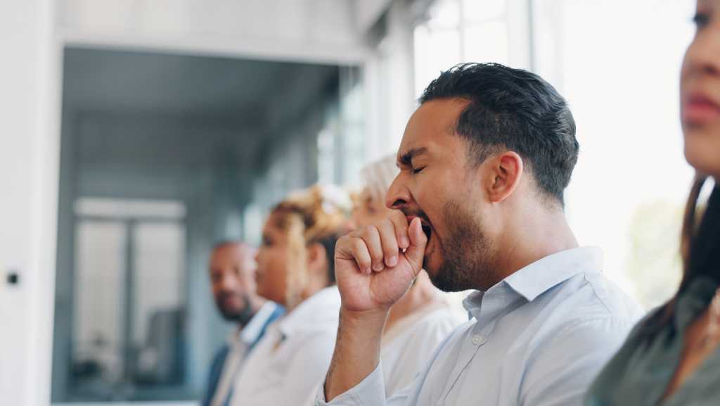 Tired, yawn and sleepless with a business man sitting in a meeting or presentation with his team for development. Yawning, exhausted and bored with a male employee suffering from insomnia at work